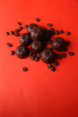 Chocolate candies and coffee beans, on red backgroundの写真素材