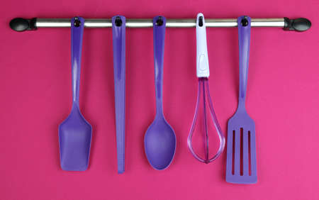 Plastic kitchen utensils on silver hooks on red backgroundの写真素材