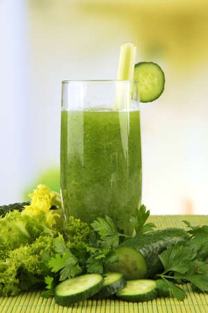 Glass of green vegetable juice and vegetables on bamboo mat on bright backgroundの写真素材