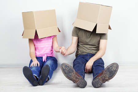 Couple with cardboard boxes on their heads sitting on floor near wallの写真素材