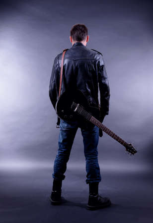 Young musician with guitar on dark color backgroundの写真素材