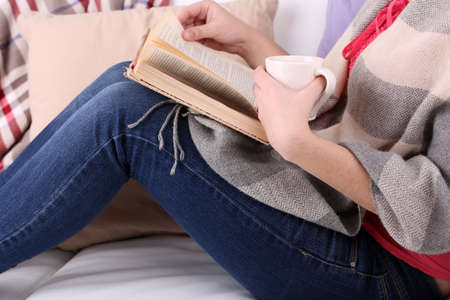 Woman sitting on sofa,  reading book and  drink coffee or tea, close-upの写真素材