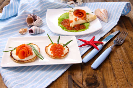 Pancakes with red caviar, salmon and mayo, green onion, on plate, on color napkin,  backgroundの写真素材