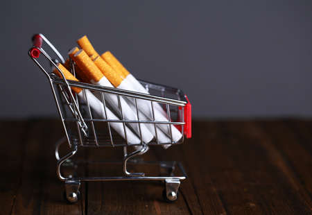 Cigarettes in shopping cart on wooden table on dark gray backgroundの写真素材