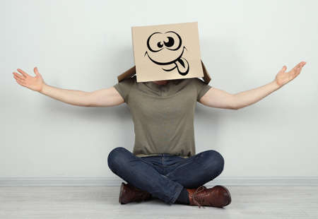 Man with cardboard box on his head sitting on floor near wallの写真素材