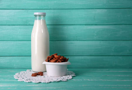 Almond milk in bottle with almonds in bowl, on color wooden backgroundの写真素材