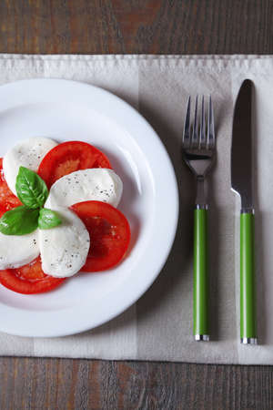 Caprese salad with mozarella cheese, tomatoes and basil on plate, on wooden table backgroundの写真素材