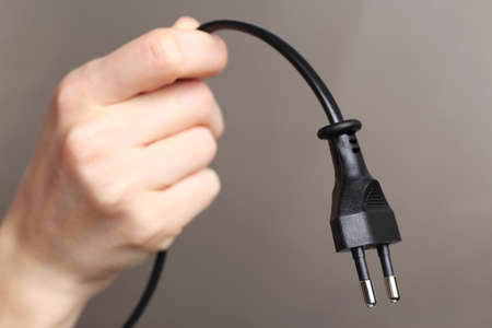 Hand holding electric plug on grey backgroundの写真素材