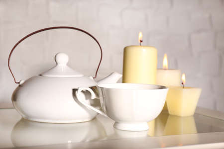 Composition with tea in cup and teapot and candles on table, on light backgroundの写真素材