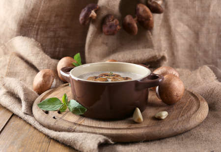 Composition with mushroom soup in pot, fresh and dried mushrooms, on wooden table, on sackcloth backgroundの写真素材