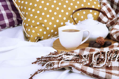 Cup and teapot with candies on wooden stand on bed close upの写真素材