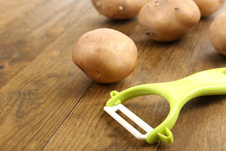 Peeler and potatoes on wooden tableの写真素材