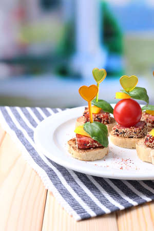 Tasty canapes with salami,tomato, pepper  and basil leaves, on plate, on wooden table, on bright の写真素材