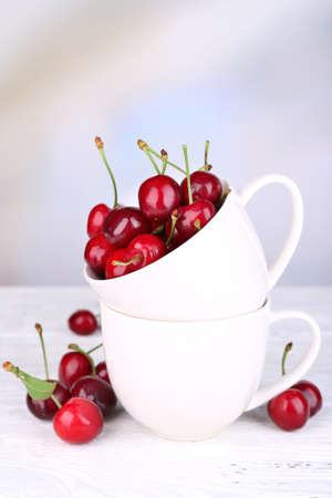 Ripe sweet cherries in cup on wooden tableの写真素材