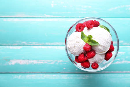 Creamy ice cream with raspberries on plate in glass bowl, on color wooden backgroundの写真素材