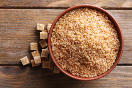 Brown sugar cubes and crystal sugar in bowl on wooden backgroundの写真素材