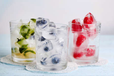 Ice cubes with mint leaves, raspberry and blueberry in glasses, on color wooden backgroundの写真素材