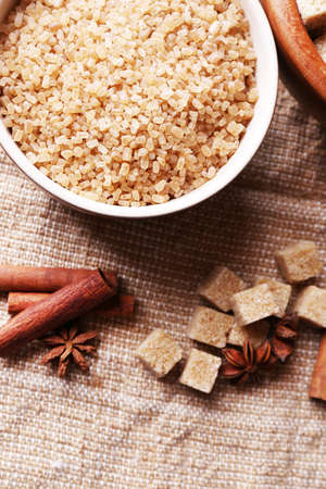 Brown sugar cubes and crystal sugar, spices in bowl on sackcloth backgroundの写真素材