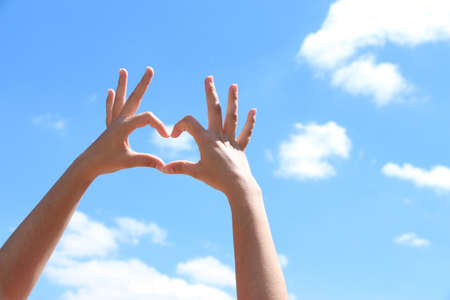 Young girl holding hands in heart shape framing on blue sky backgroundの写真素材