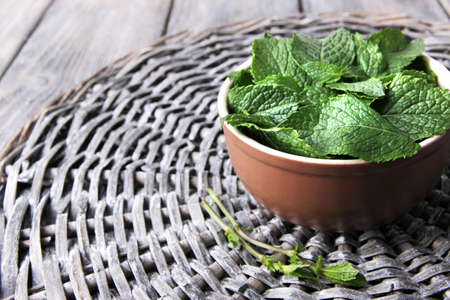 Brown round bowl of fresh mint leaves on a stand on wooden tableの写真素材