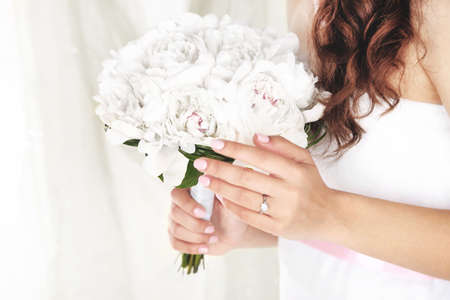 Bride holding wedding bouquet of white peonies on light backgroundの写真素材