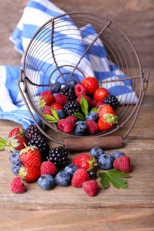Ripe sweet different berries in metal basket, on old wooden tableの写真素材