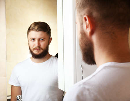 Young man shaving his beard in bathroomの写真素材