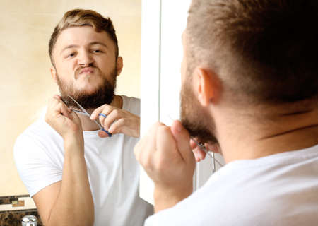Young man shaving his beard in bathroomの写真素材