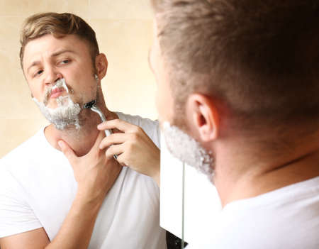 Young man shaving his beard in bathroomの写真素材