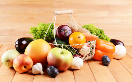 Fresh organic fruits and vegetables in wicker basket on wooden の写真素材