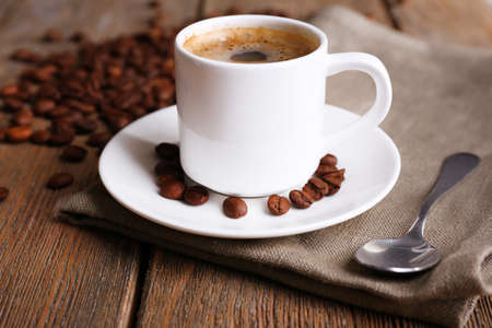 Cup of coffee and coffee beans on napkin on wooden backgroundの写真素材