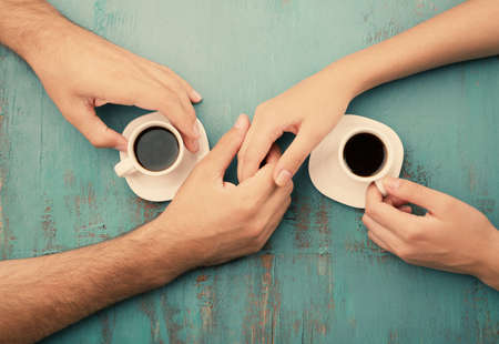 Coffee cups and holding hands at the wooden tableの写真素材