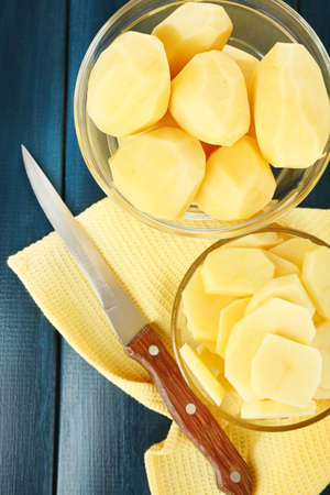Raw peeled and sliced potatoes in glass bowls  on color wooden backgroundの写真素材