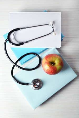 Medical stethoscope with apple on books on wooden tableの写真素材
