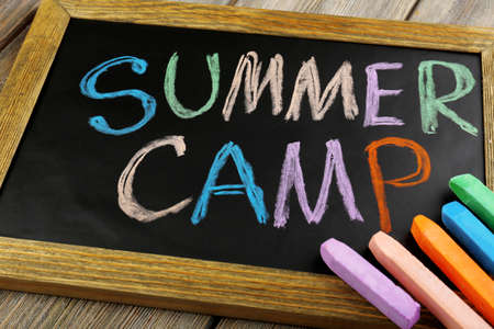 Text Summer camp written with chalk on chalkboard, and some chalk sticks of different colorsの写真素材