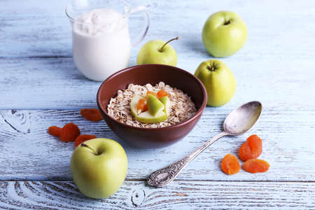 Bowl of oatmeal, dried apricots, apples and yogurt on blue wooden backgroundの写真素材