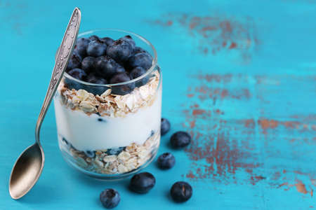Healthy breakfast - yogurt with  blueberries and muesli served in glass jar, on color wooden backgroundの写真素材