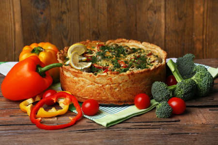 Vegetable pie with broccoli, peas, paprika, tomatoes and cheese on napkin, on wooden backgroundの写真素材