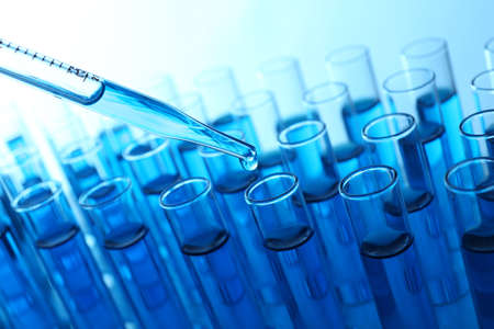 Pipette adding blue fluid to the one of test-tubes on light background