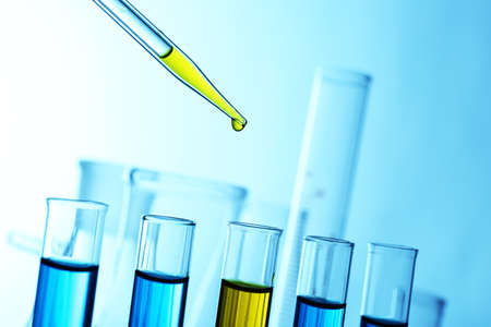 Pipette adding yellow fluid to one of several test-tubes with flasks on light backgroundの写真素材