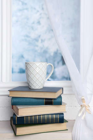 Composition of books and cup on the windowsill on light backgroundの写真素材