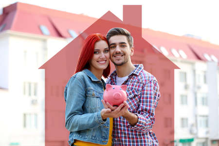 Loving couple with piggy bank near apartment houseの写真素材