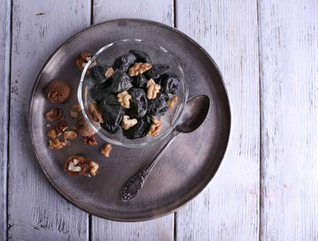 Metal tray with glass bowl of prunes and walnuts, shell and spoon on color wooden backgroundの写真素材