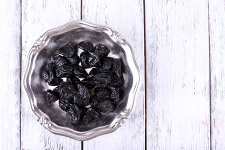 Metal plate of prunes on color wooden backgroundの写真素材