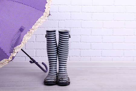 Dirty wellington boots with umbrella on floor in roomの写真素材