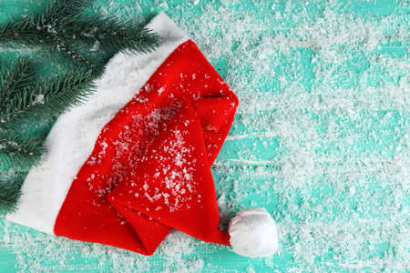 Santa red hat with fir-tree branch and snowflakes on color wooden backgroundの写真素材