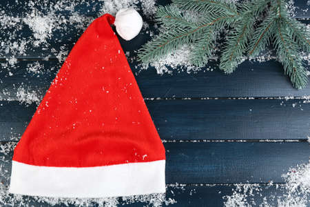 Santa red hat with branch of fir-tree and snowflakes on color wooden backgroundの写真素材