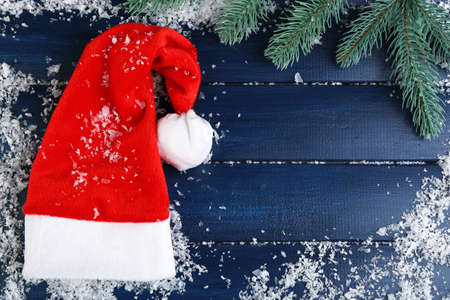 Santa red hat with branch of fir-tree and snowflakes on color wooden backgroundの写真素材