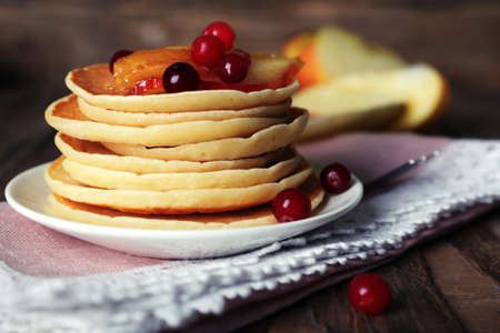 Stack of delicious pancakes with slices of apple and berries on plate and napkin on wooden backgroundの写真素材