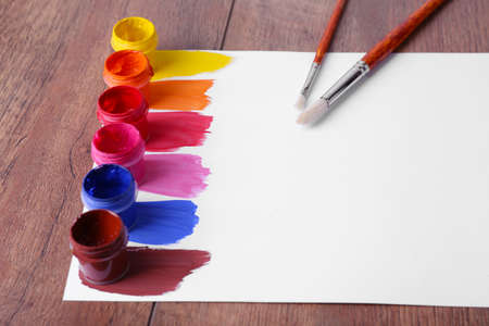 Colorful paint strokes with brush and paint cans on white sheet of paper on wooden table backgroundの写真素材